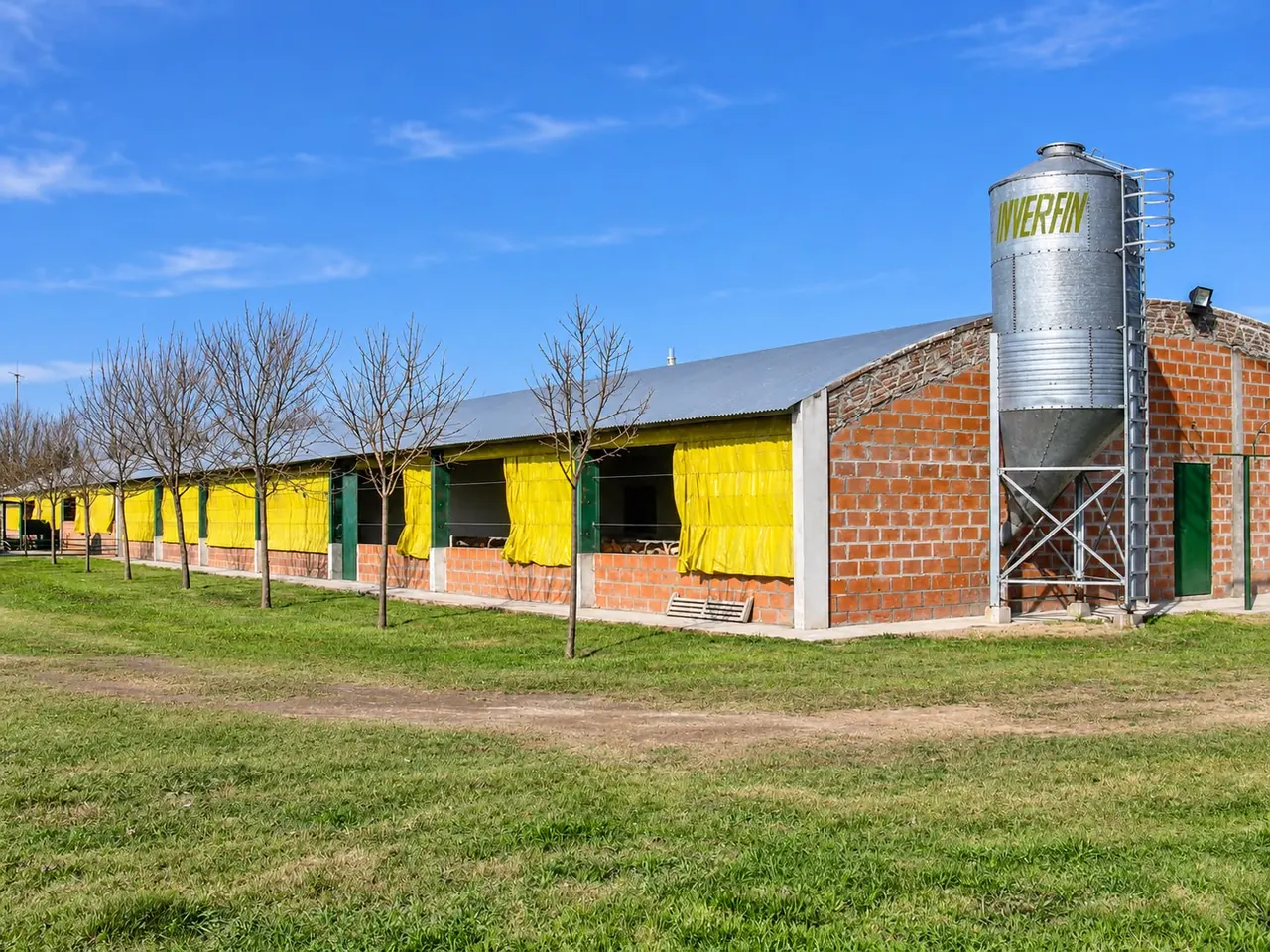 Galpón de ladrillo con silo de alimento y campo alrededor
